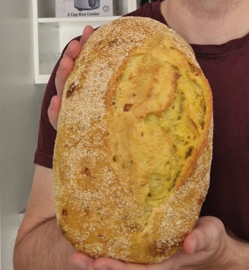 Image of a freshly baked turmeric sourdough loaf from Volare. The bread has a vibrant golden-yellow color, reflecting the turmeric infusion, with a rustic crusty exterior. The loaf is held by a person’s hands.